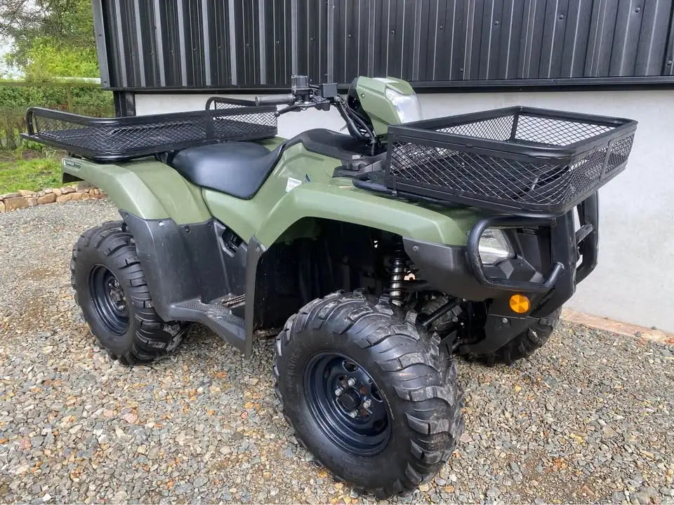 Olive green honda atv with black mesh cargo baskets and rugged off-road tires.