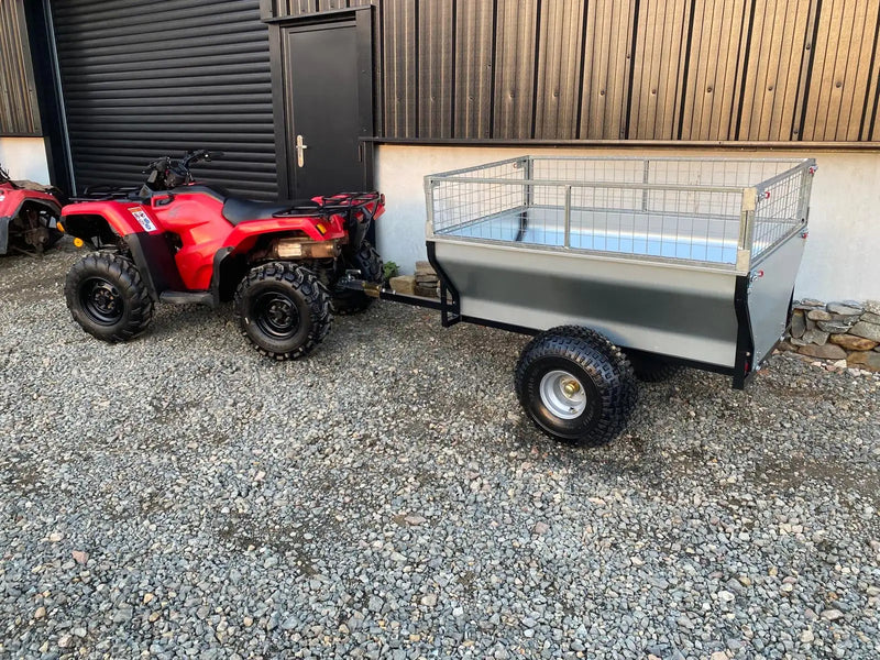 Red atv with black tires and handlebars, towing a gray metal utility trailer featuring wire mesh sides.
