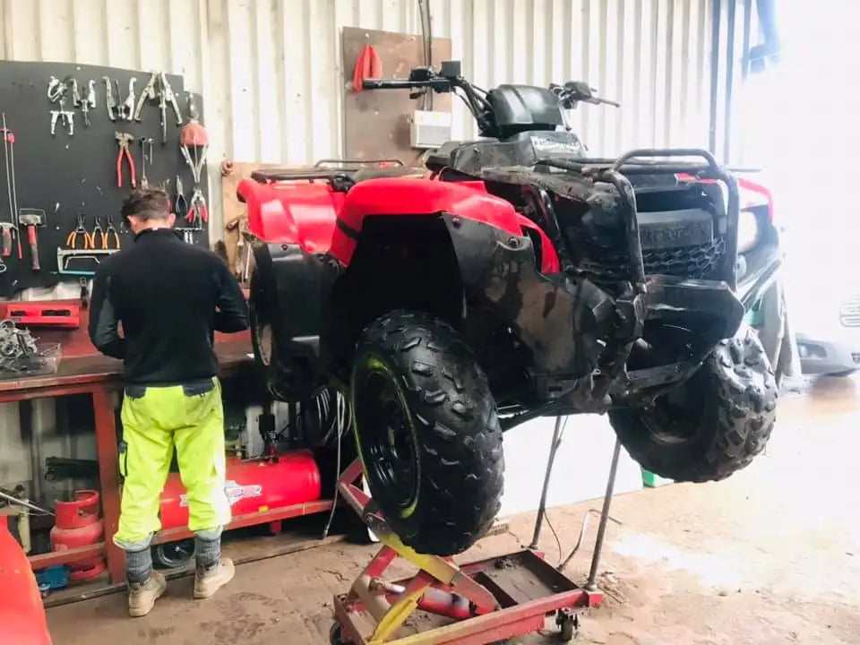 Red and black honda atv with rugged tires and protective front bumper.