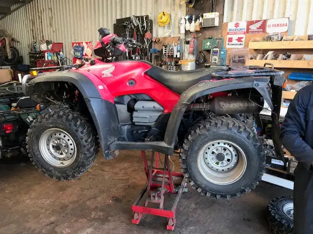 Red honda atv with black fenders and tires, featuring a rugged design typical of off-road vehicles.