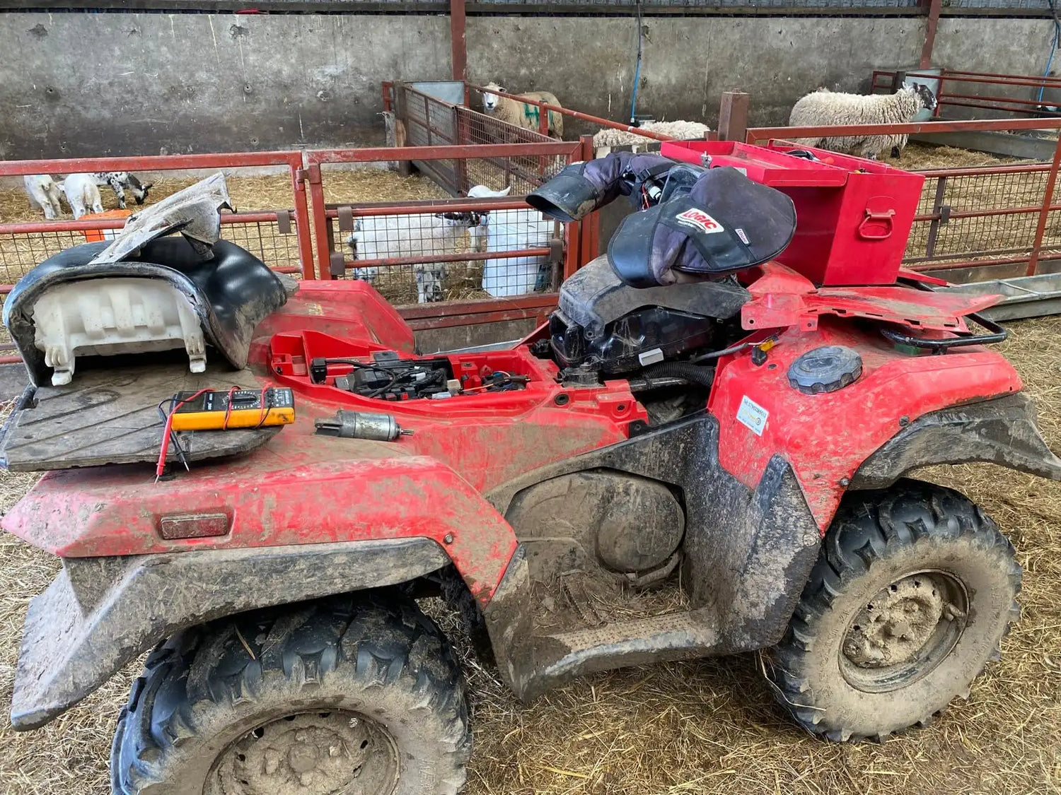Red, muddy honda atv with black tires and a partially disassembled seat.