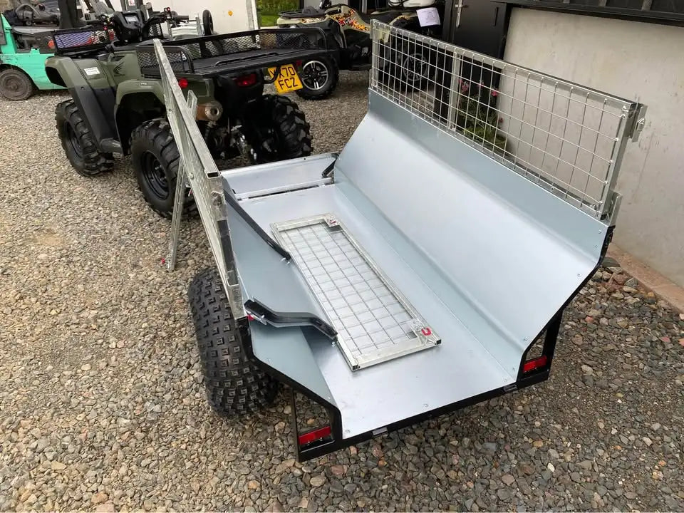 Silver metal utility trailer with a mesh grid on the back and side, featuring black rubber tires.